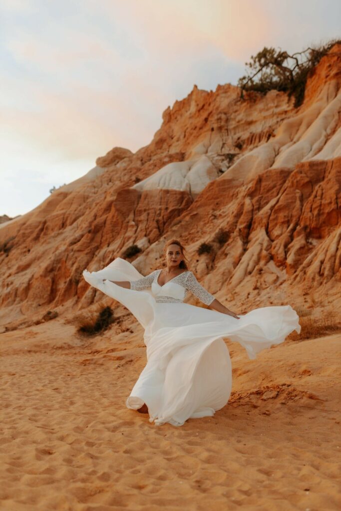 Mariée en robe blanche tenant son voile au pied de falaises