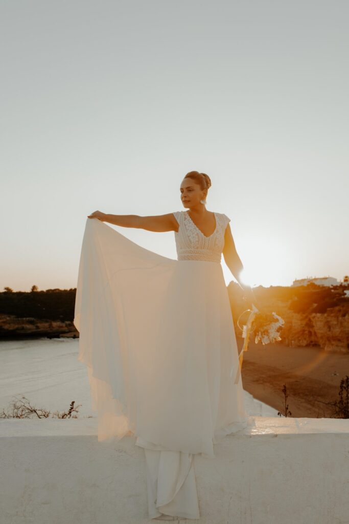 Mariée tenant le voile de sa robe au coucher du soleil