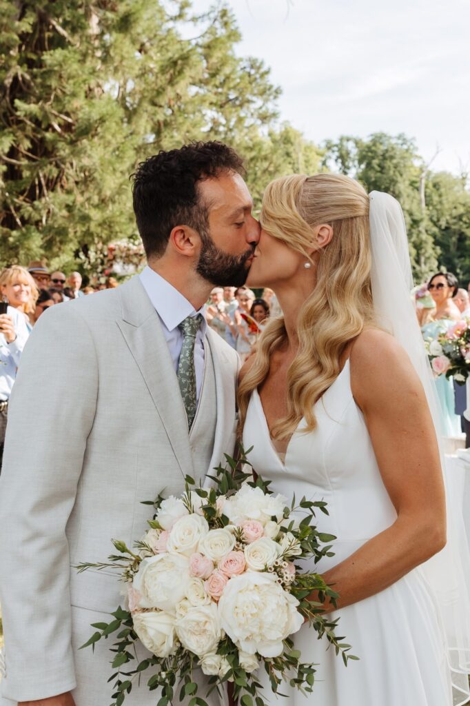 Mariés s’embrassant, la mariée tenant un bouquet de fleurs blanches