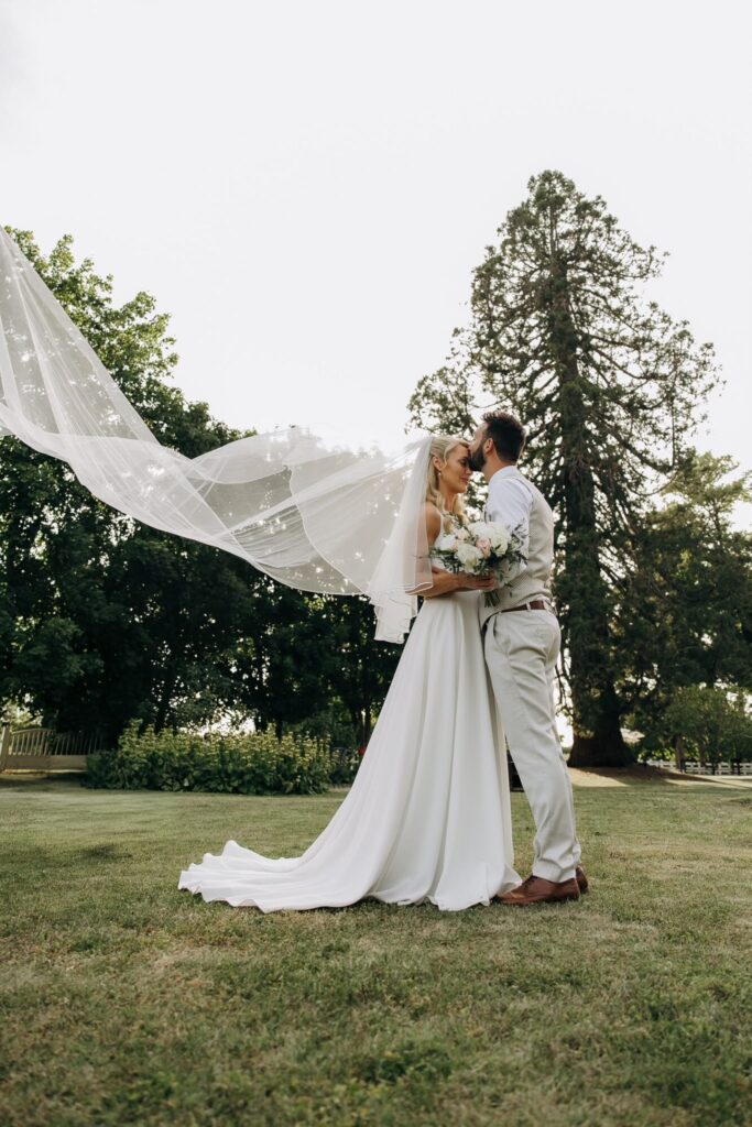 Mariés enlacés sur une pelouse, voile de la mariée au vent